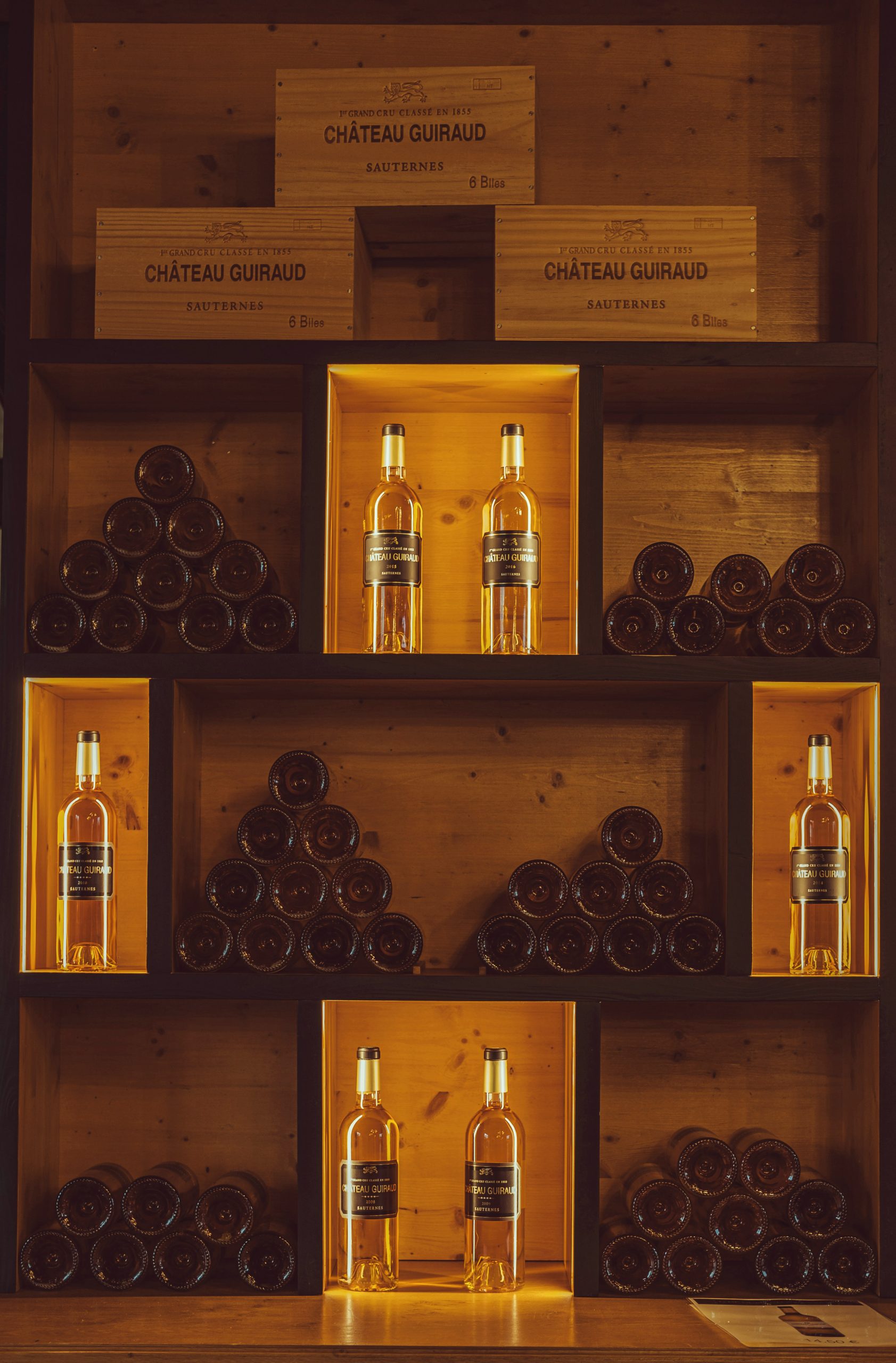 bottles of château guiraud sauternes wine displayed in illuminated wooden cellar shelves